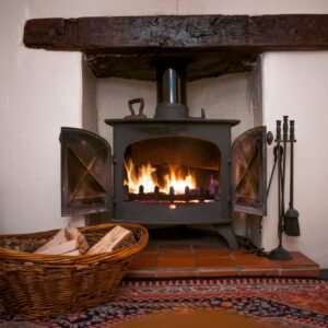 a cast iron wood stove with a fire going and a basket of wood beside it