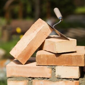 a stack of bricks with some mortar in between with a couple loose bricks and a trowel on top